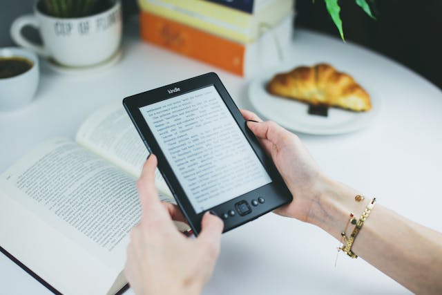 Oseba drži kindle bralnik in kavo