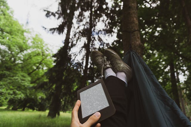 Oseba v viseči mreži drži kindle bralnik