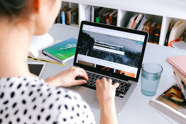 Person-Using-Macbook-Pro-On-White-Table-with-a-Glass-of-Water