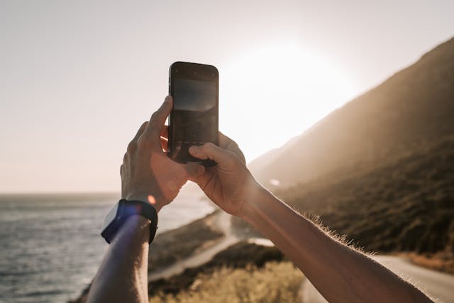 Person-taking-a-photo-of-the-sunset-over-the-coastline-with-a-smartphone.jpg