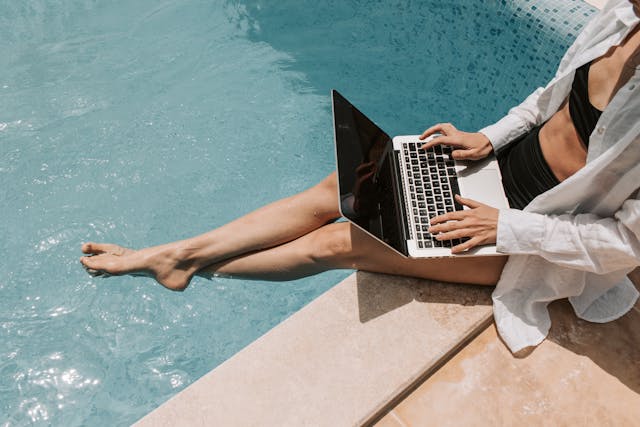 ženska sedi ob bazenu in uporablja prenosni računalnik.jpg